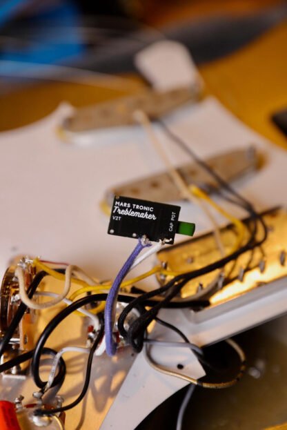 The Mars-Tronic Treblemaker wired into a strat style pickguard. The wires suspend the Treblemaker up above the white pickguard. The Treblemaker logo can be seen on the rear of the circuit board.