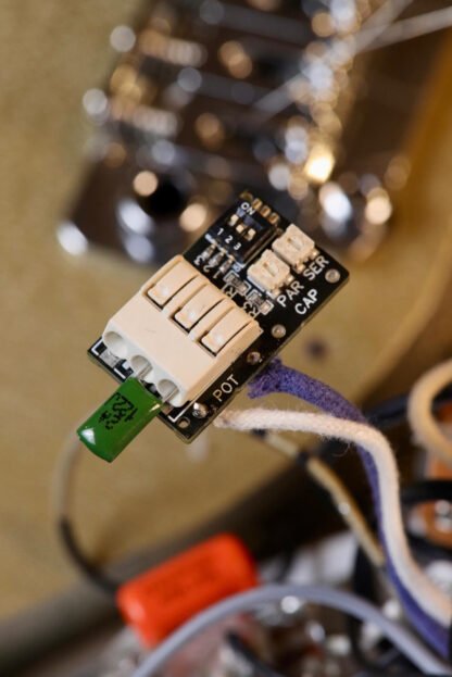 Close-up of the Mars-Tronic Treblemaker with a visible capacitor in push-fit terminals and blue-and-white cloth wires, against a blurred backdrop of guitar electronics.